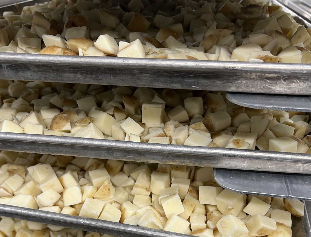 Peeled and chopped potatoes are placed on baking sheets in a speed rack.